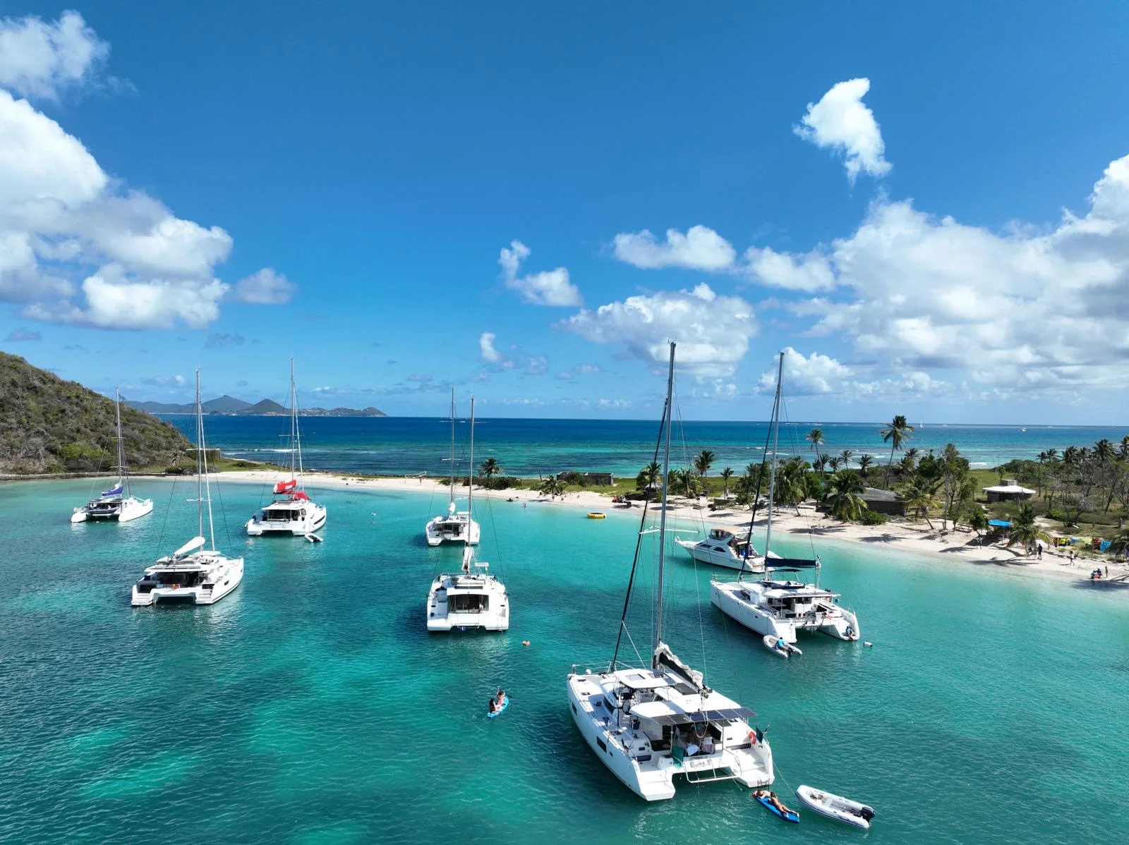 Plusieurs catamarans au mouillage devant une plage des Caraïbes